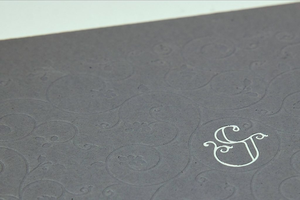 Monograma estampado sobre papel gris con relieve