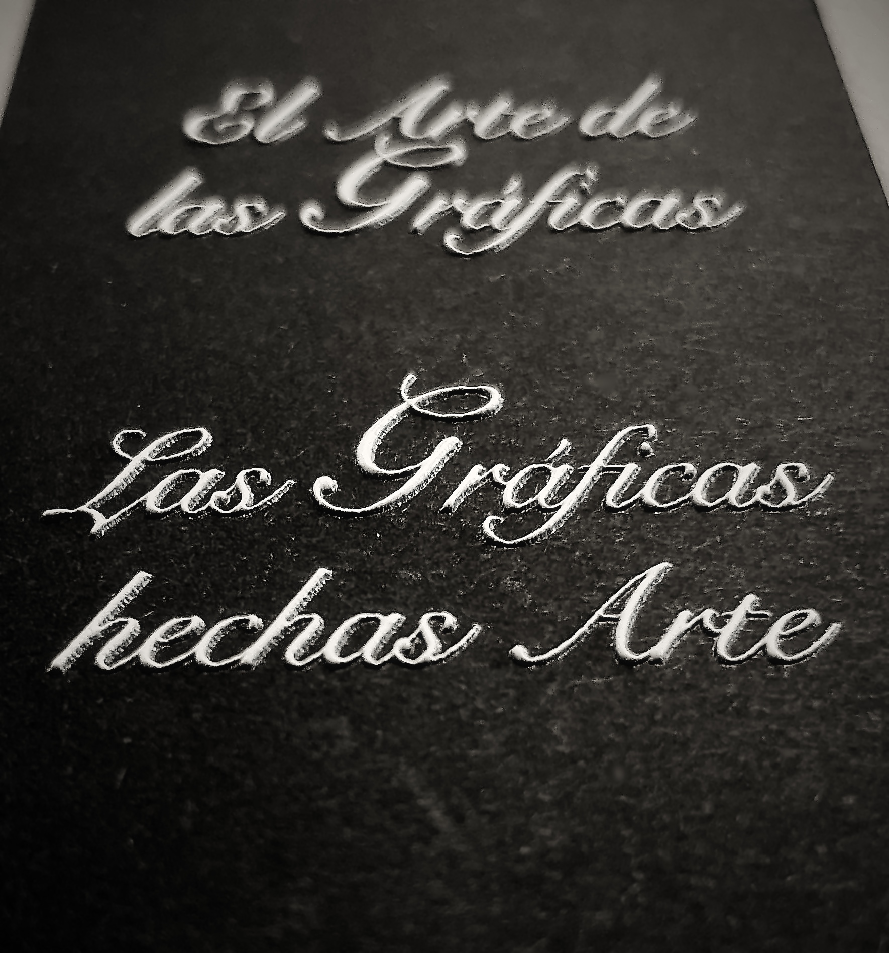 Black card with the motto “El Arte de las Gráficas, las Gráficas hechas Arte” in raised silver